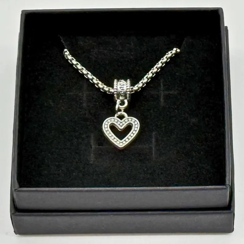 Silver open-heart pendant with beaded detailing on a box chain, set in a black gift box, photographed in the Robert Anthony Art home studio