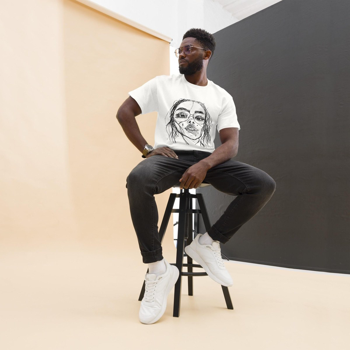 Model seated on a stool wearing a white t-shirt printed with a hand-drawn Muse portrait sketch by Robert Anthony