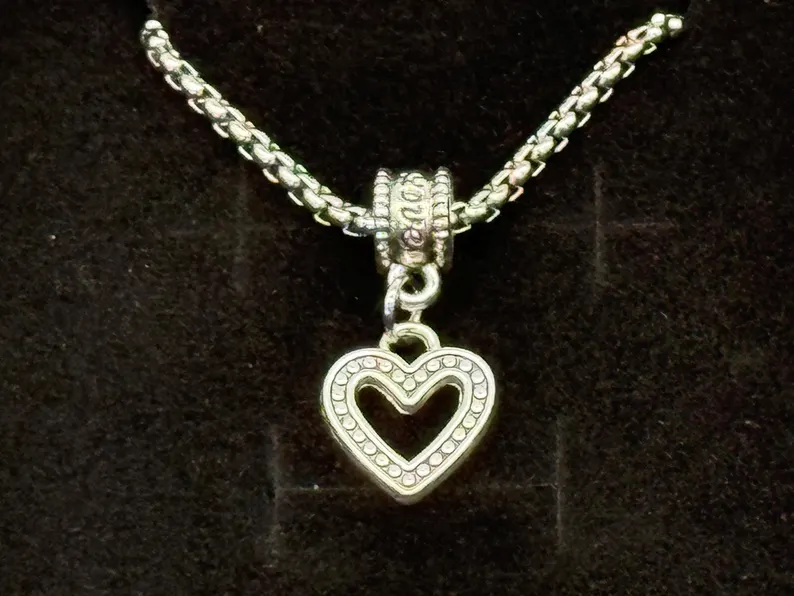 Macro close-up of a silver open-heart pendant with beaded edge and decorative bail on a box chain