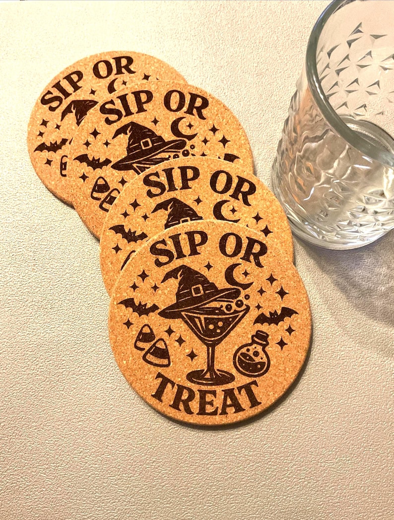 Four laser etched cork coasters with a Sip or Treat witch hat cocktail design fanned out beside a cut-glass tumbler