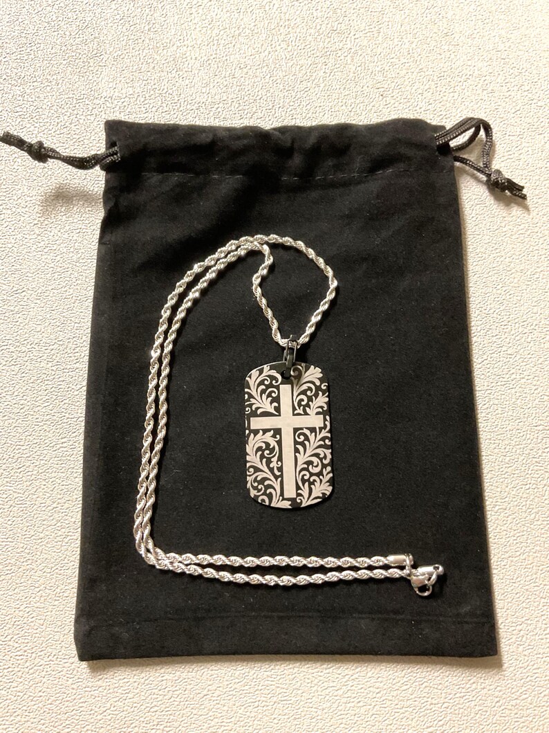 Custom laser engraved crucifix cross aluminum dog tag necklace displayed on a black velvet drawstring gift pouch, ready to ship as a gift — made by Robert Anthony Art in Vacaville, California