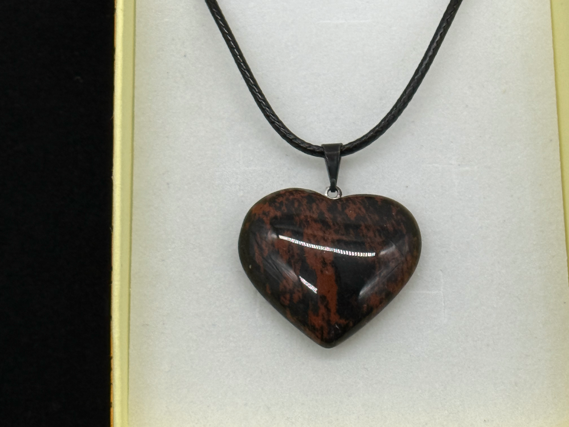 Polished mahogany obsidian heart pendant on a black cord, showing warm red-brown and black banding
