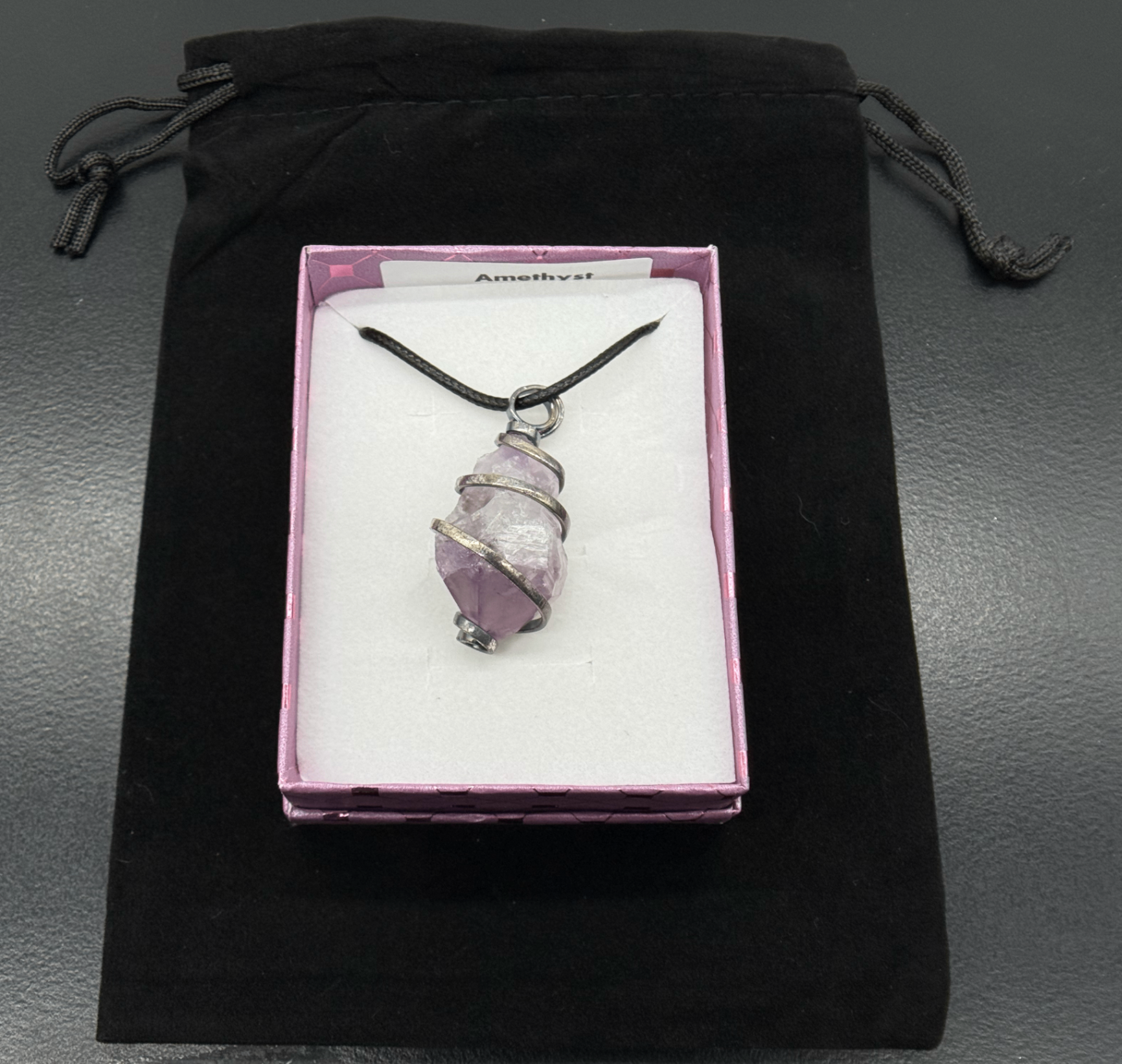 Raw amethyst point pendant hand wrapped in a silver wire spiral, resting in a pink gift box