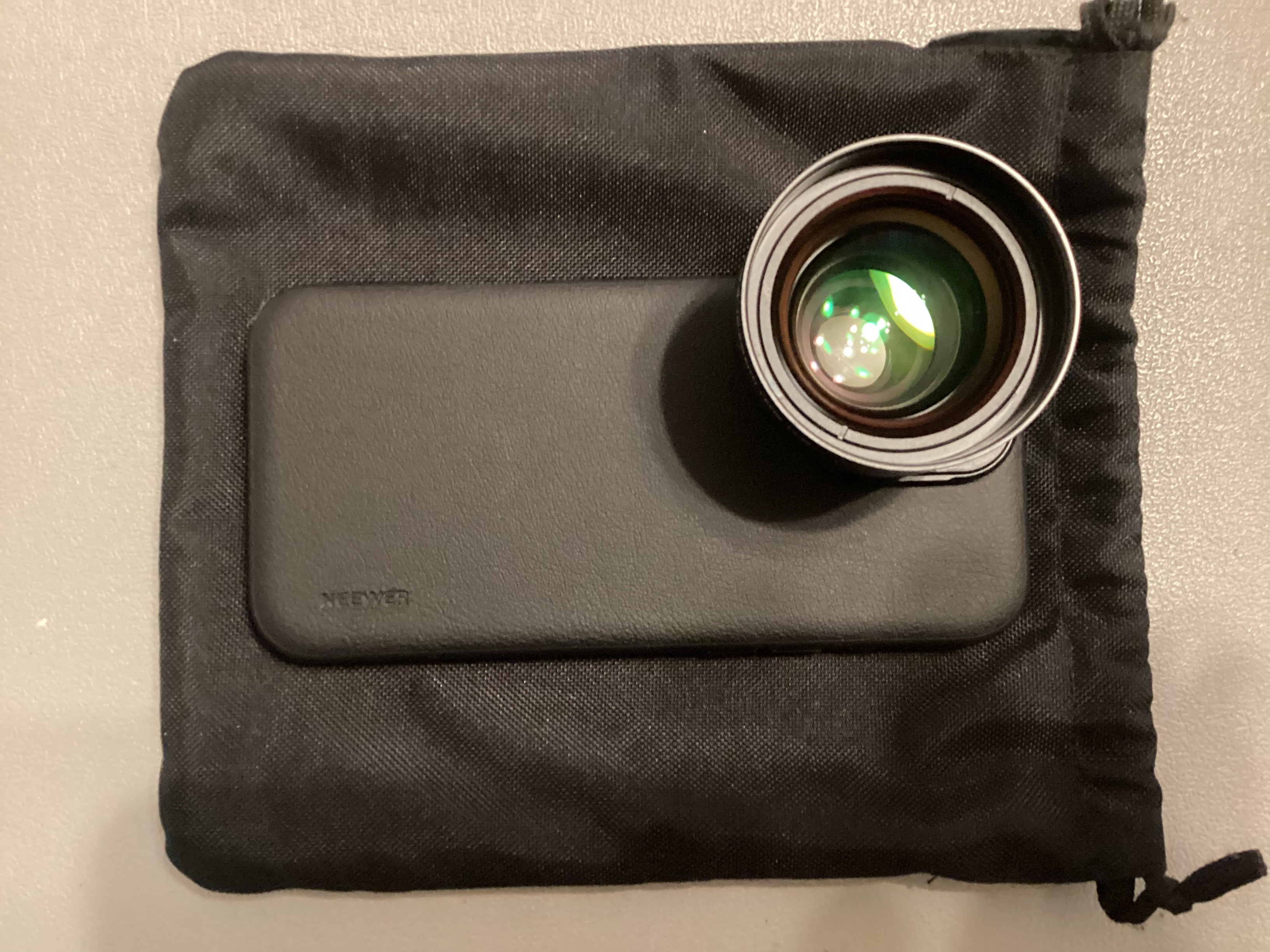 Clip-on iPhone wide-angle lens and phone case resting on a black drawstring storage pouch