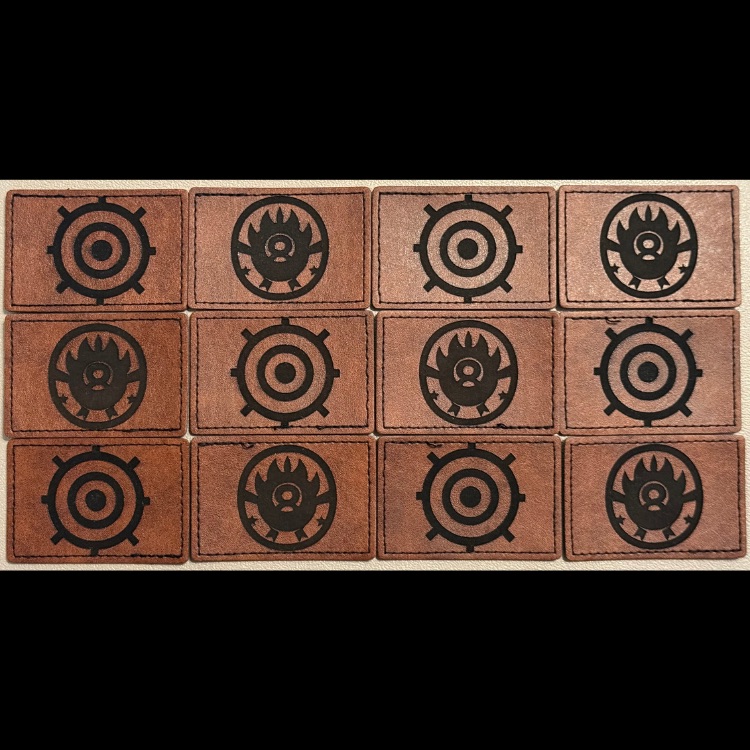 Twelve laser engraved brown leather patches laid out in a grid, each burned with a dark circular emblem design — custom leather patch engraving by Robert Anthony Art in Vacaville, California