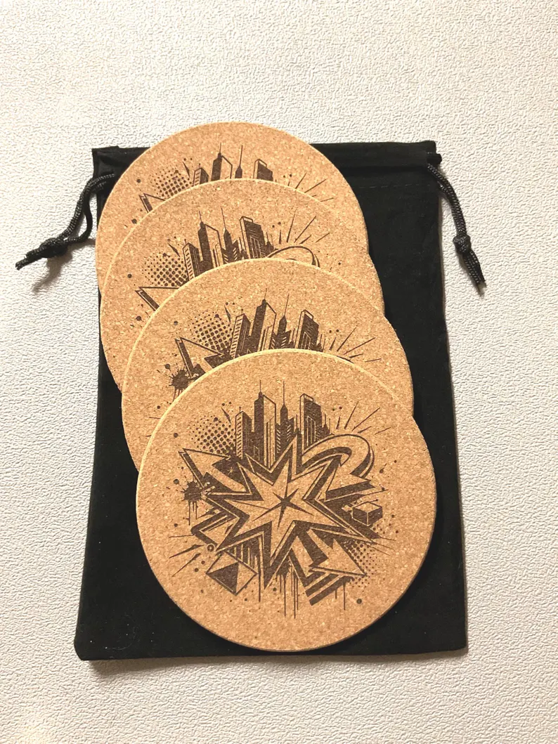 Set of four laser etched cityscape cork coasters beside a black velvet drawstring pouch on a light surface