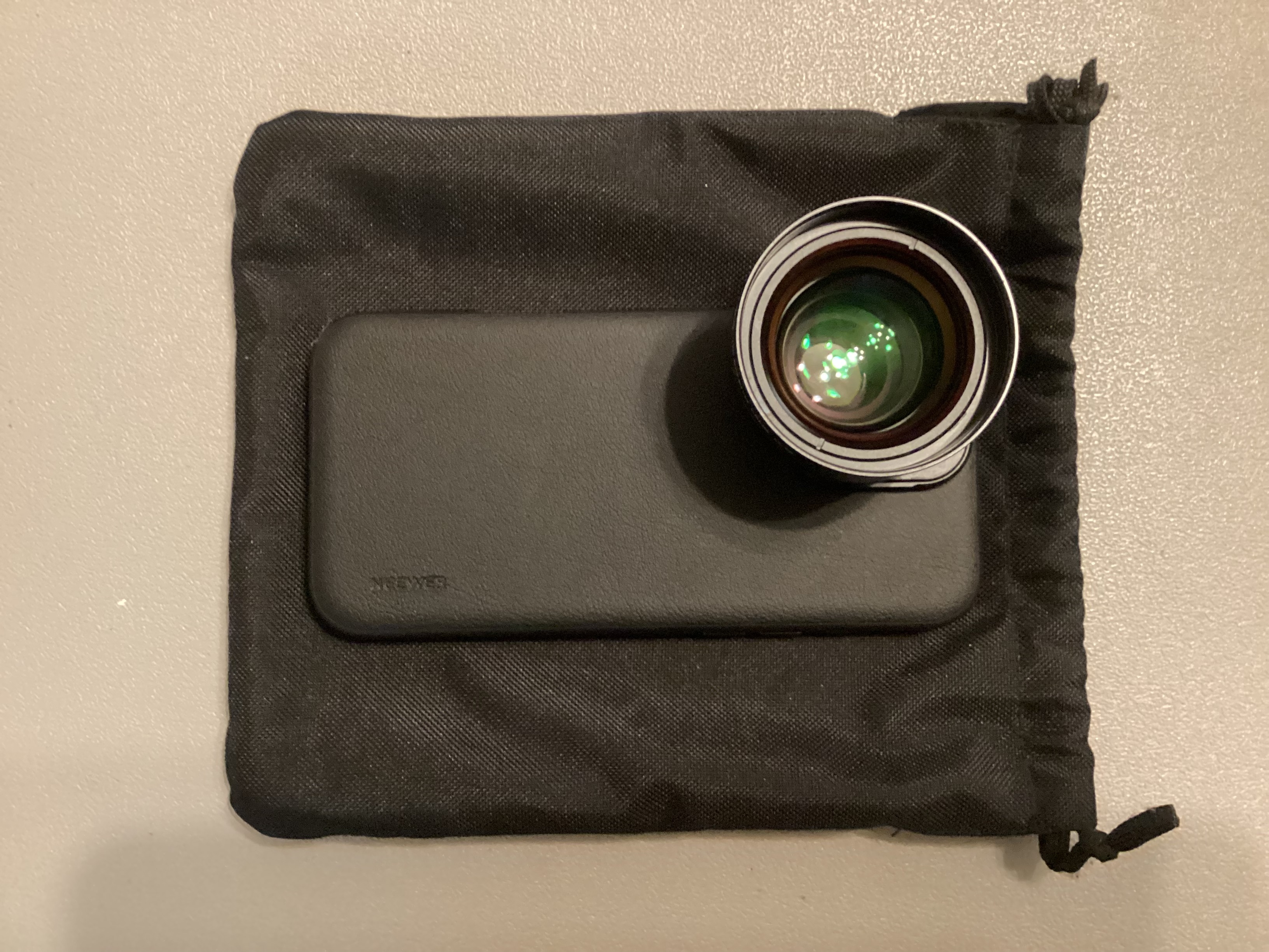 NEEWER HD 65mm telephoto phone lens mounted to a phone case and resting on its black drawstring pouch