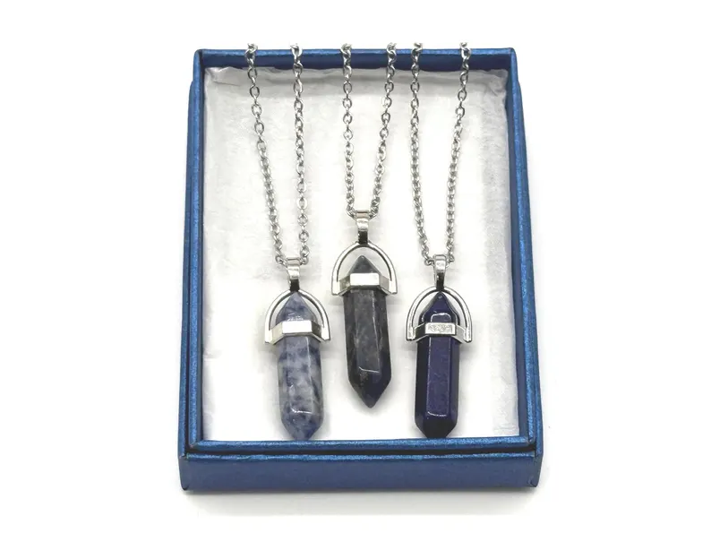 Three natural stone bullet-point pendants — sodalite, dark labradorite, and lapis lazuli — arranged in a blue gift box, photographed in the Robert Anthony Art home studio