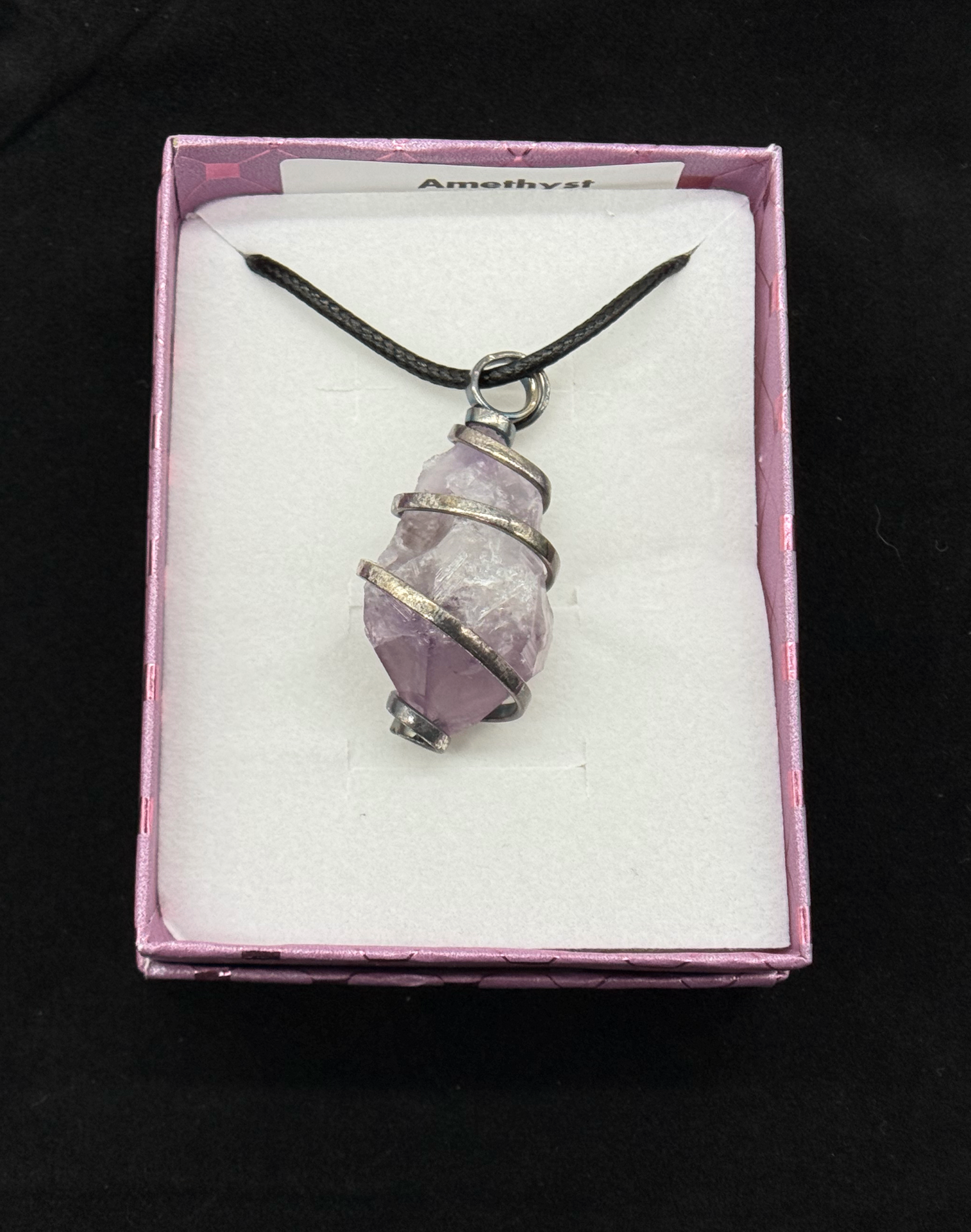 Close-up of a raw amethyst crystal wrapped in a silver spiral wire cage