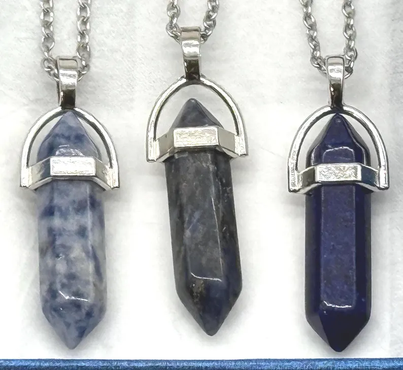 Close-up of three natural stone crystal point pendants in silver settings — sodalite, dark stone, and lapis lazuli