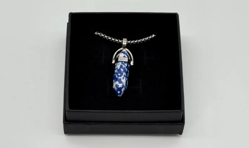 Sodalite crystal point pendant photographed at an angle inside a black gift box