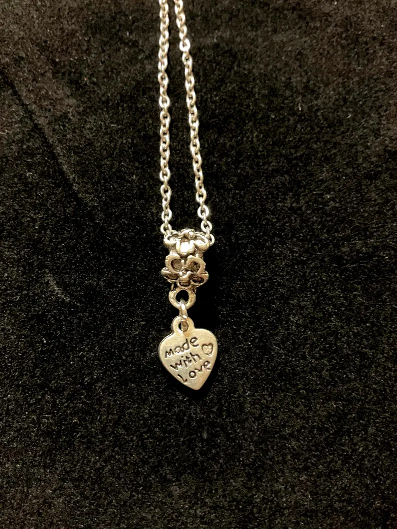 Silver 'made with love' heart charm hanging from a delicate chain on black velvet