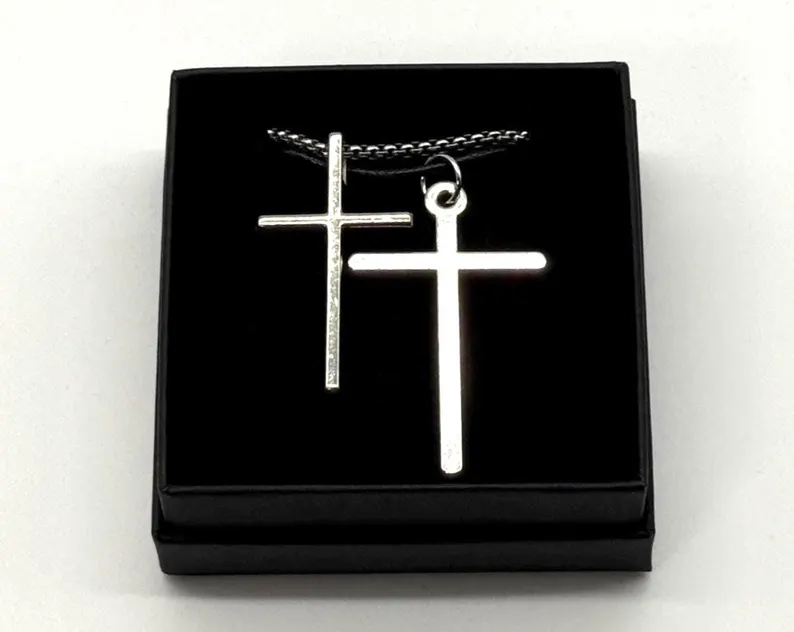 Overhead shot of two silver cross pendants catching light inside a black gift box