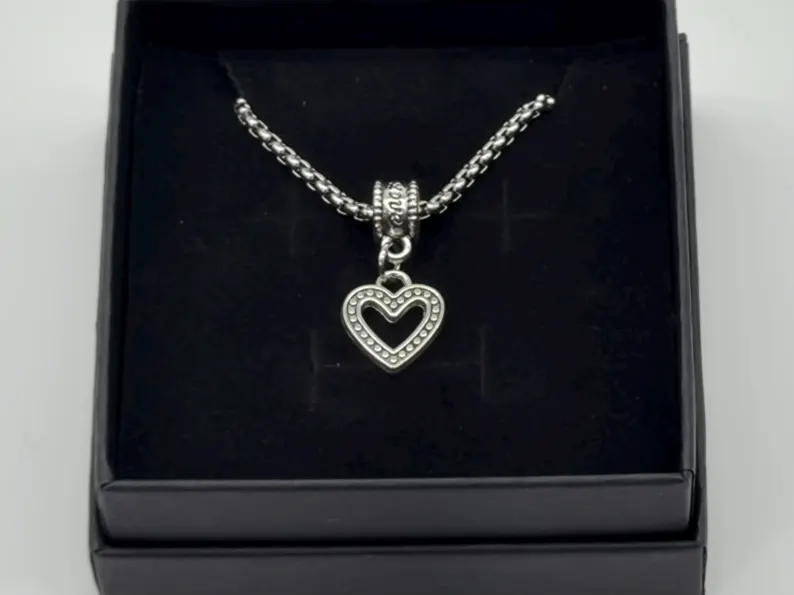 Silver heart pendant on a box chain resting inside a black gift box, overhead angle