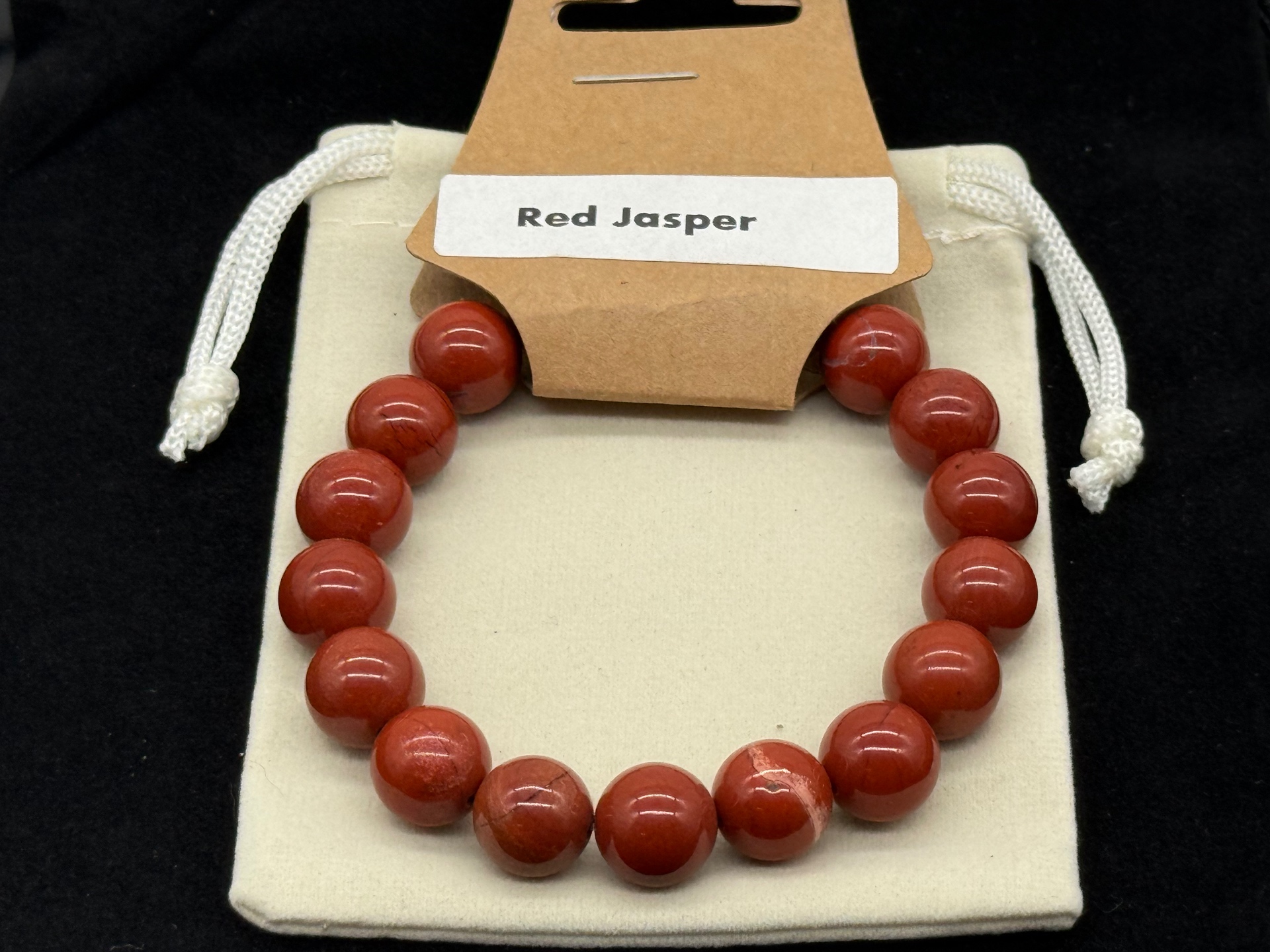 Polished red jasper bead bracelet on a cream pouch, photographed in-studio by Robert and Angela