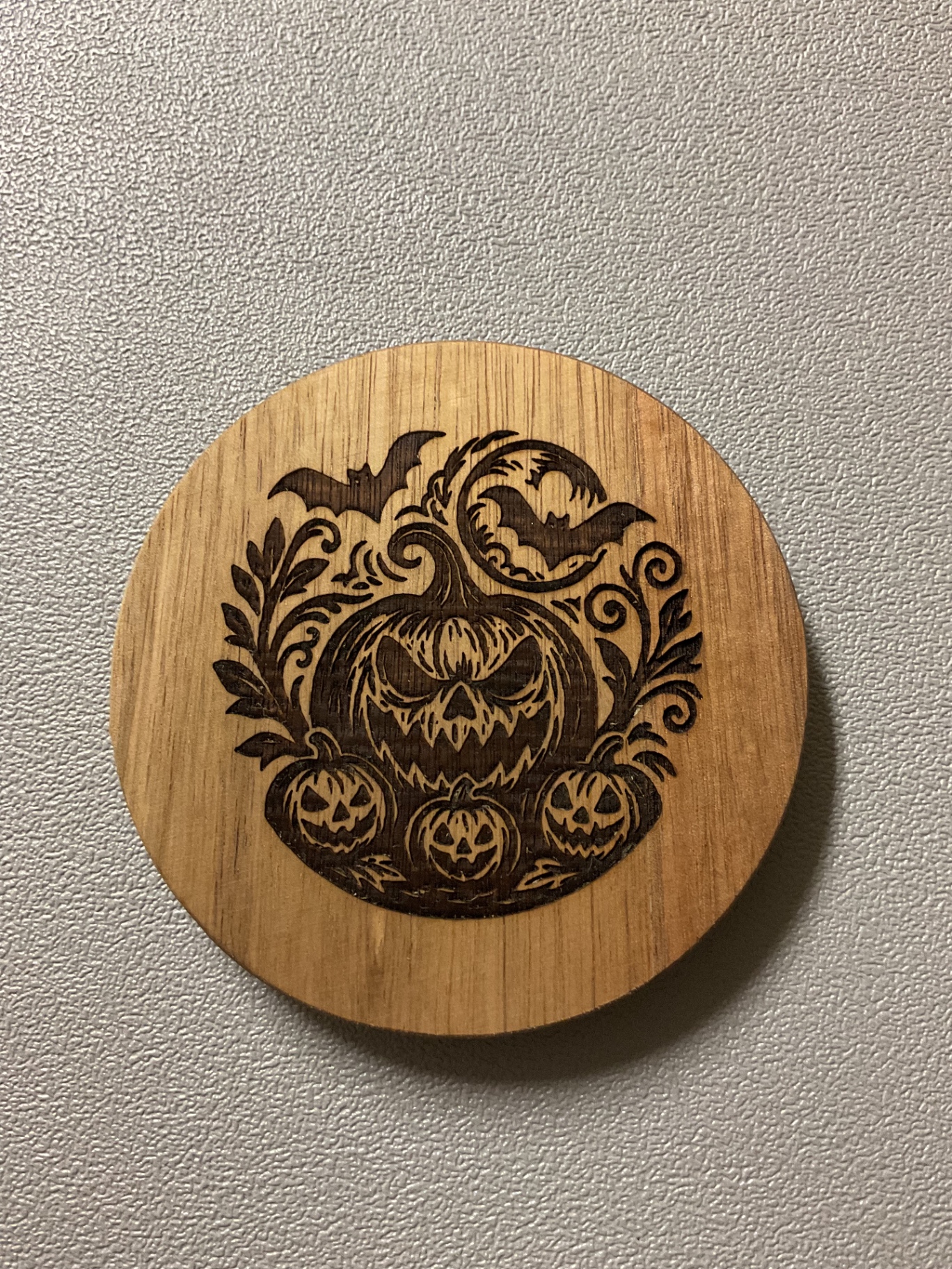 Single wood coaster laser-etched with a detailed jack-o'-lantern and bat design