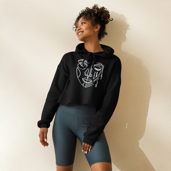 Model wearing a black cropped hoodie printed with a white One-Eyed Muse hand-drawn face design