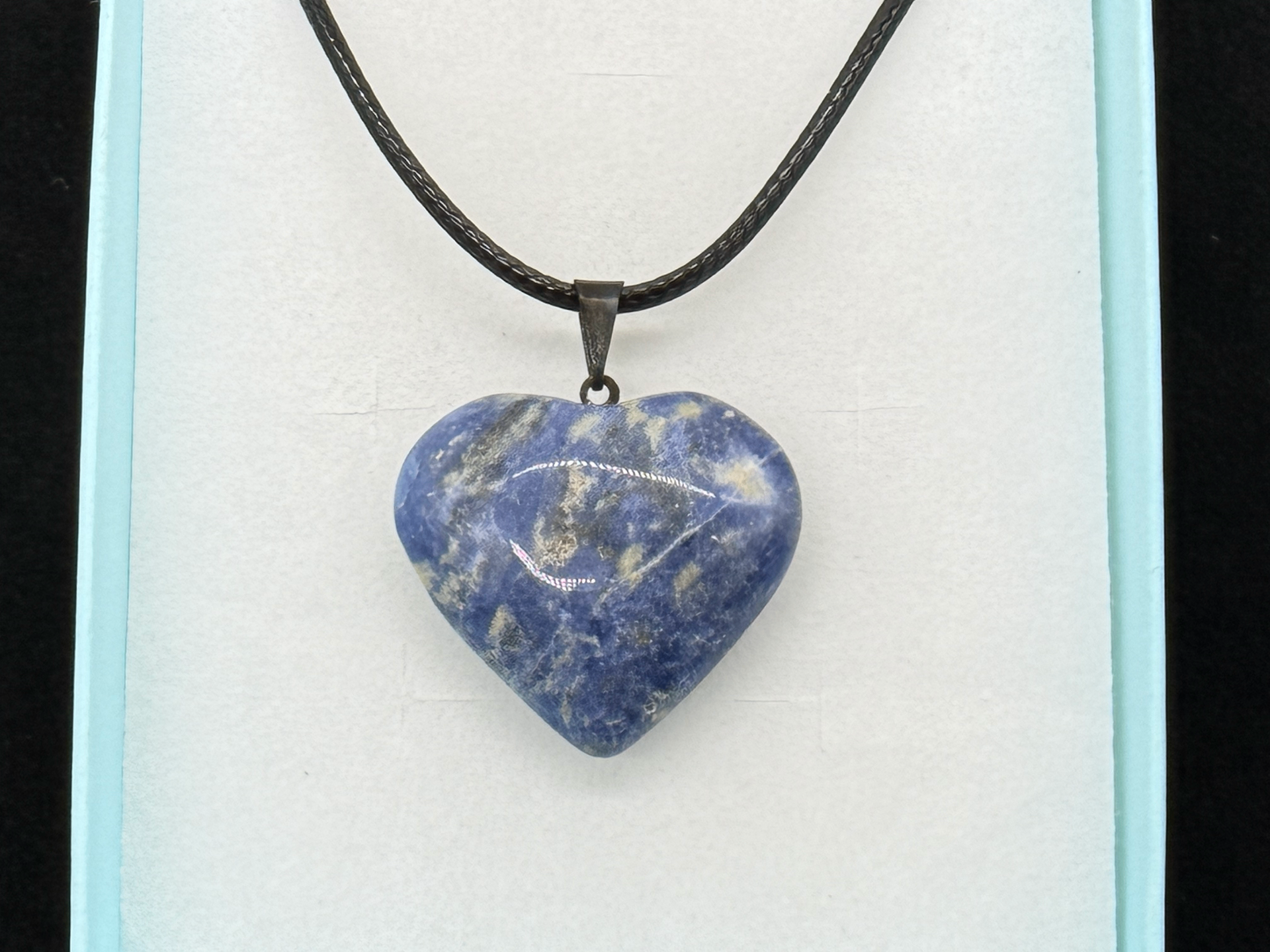 Polished sodalite heart pendant on a black cord, photographed in-studio by Robert and Angela