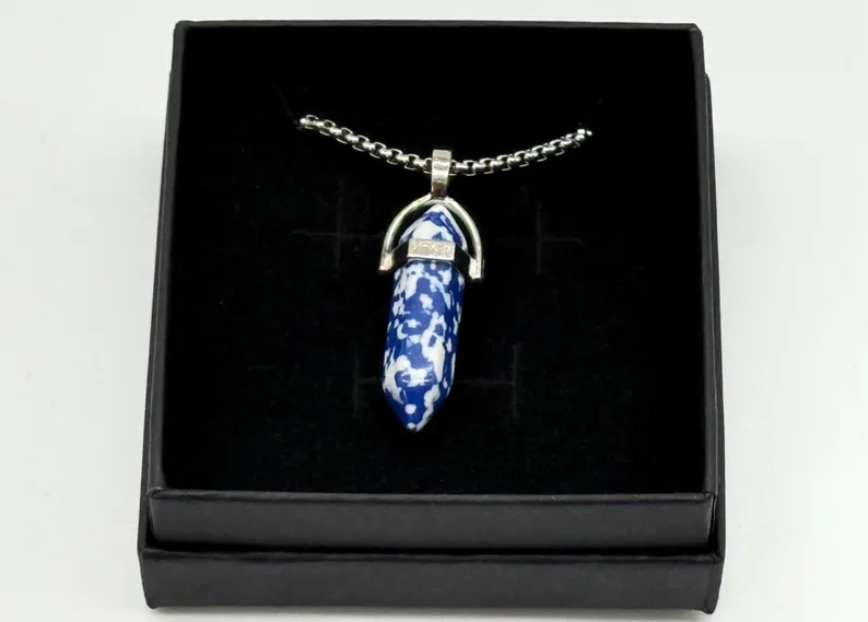 Sodalite crystal point pendant centered inside a black gift box, overhead studio shot
